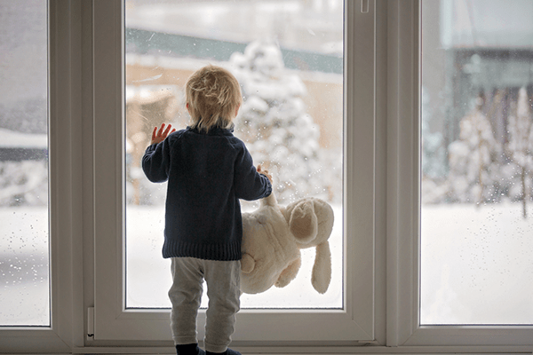 Ett litet barn som håller i sin mjukiskanin kikar ut genom en glasdörr på den snöbelagda tomten utanför