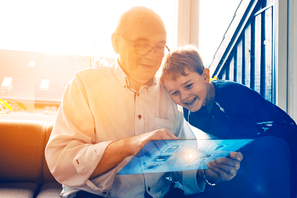 En äldre man visar ett litet barn något på en interaktiv glasskärm.