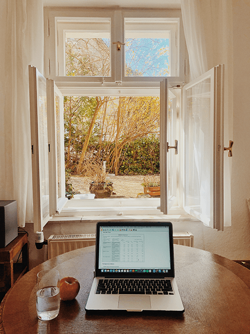En dator på ett bord med ett öppet fönster i bakgrunden