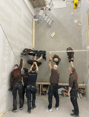 5 män monterar en lutande spegel på vägg