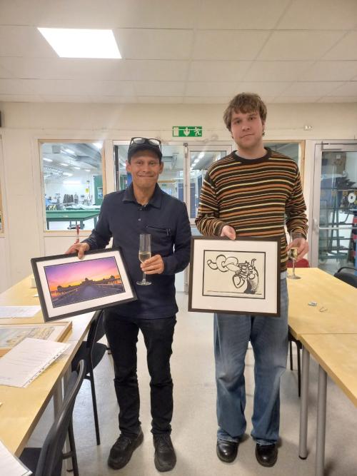 Två män håller i varsin inramning och tittar in i kameran