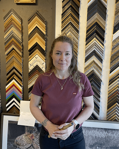 Kvinna i röd t-shirt framför en vägg med tavelramar