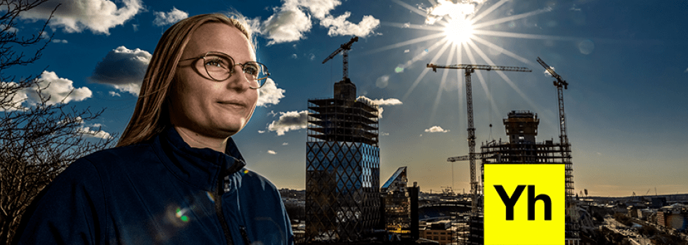 En kvinna till vänster i bild i förgrunden. I bakgrunden lyser solen mot blå himmel över en byggnad med glasfasad under konstruktion Foto: Sören Håkanlind.