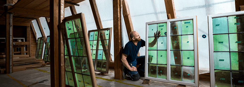 En glasmästare står på knä och håller upp ett vackert gammalt fönster med gröna glas