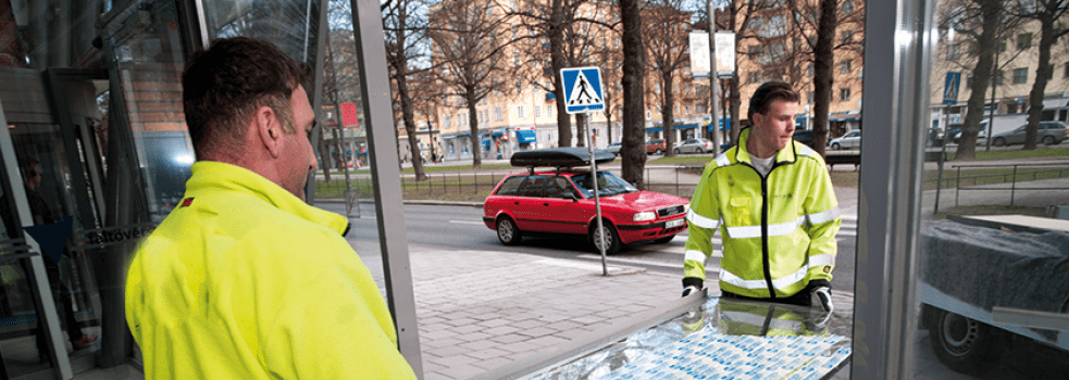 Två glasmästare bär ut en trasig glasruta som ska restaureras