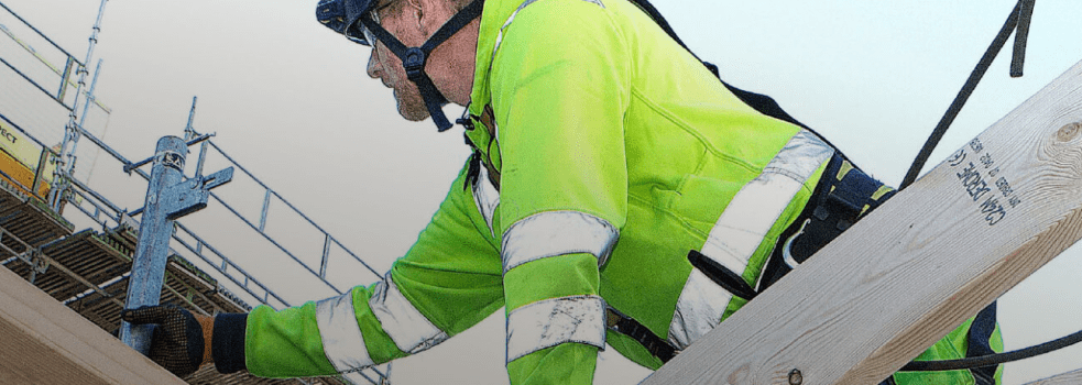 En byggnadsarbetare är säkrad med sele i en lina. 