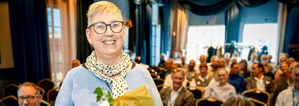 kvinna i blå tröja och glasögon tittar leendes in i kameran