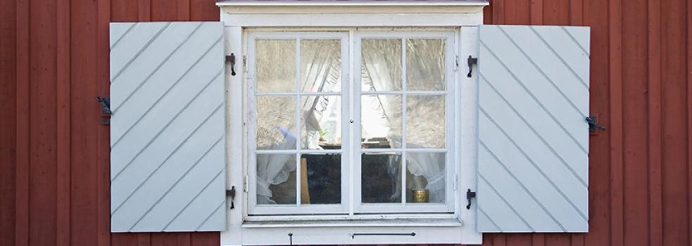 Ett fönster med vita luckor mot en röd furuvägg