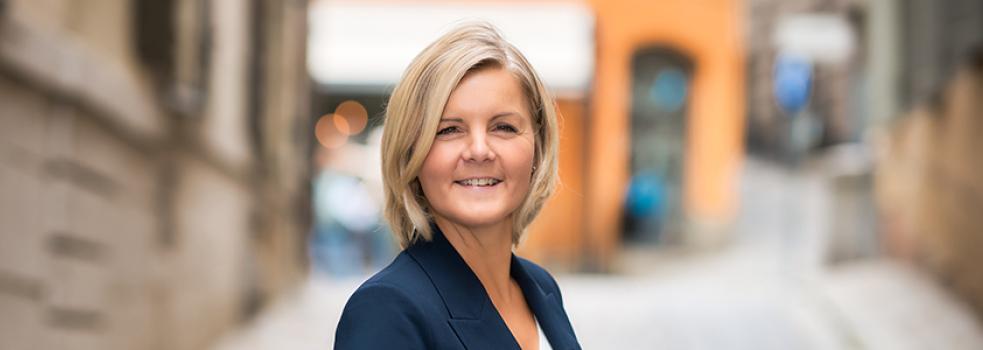 Kvinna i blont hår och kavaj tittar in i kameran
