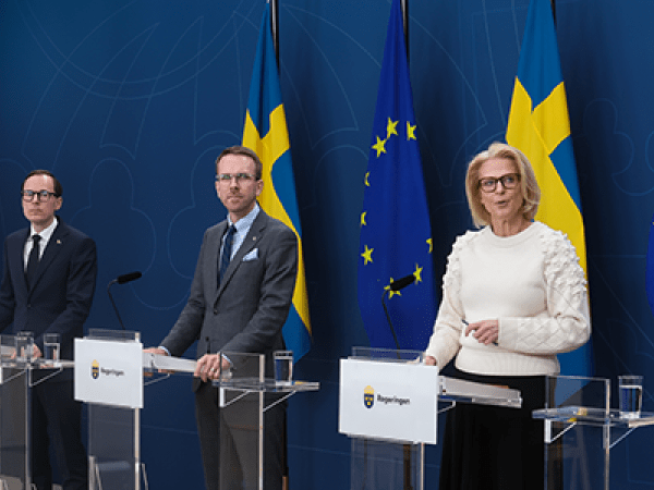tre män och en kvinna står vid talarpodier framför svenska- och Eu-flaggor