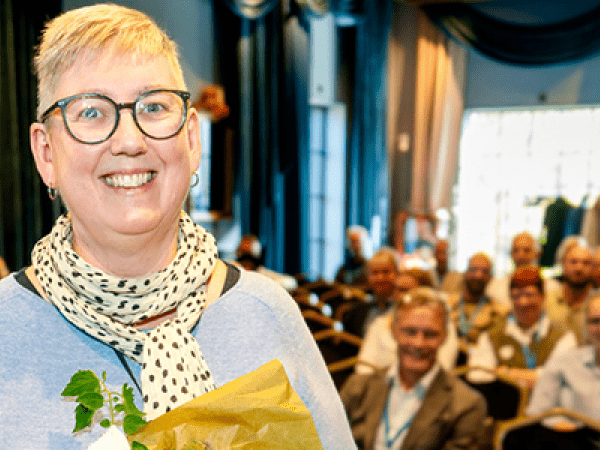 kvinna i blå tröja och glasögon tittar leendes in i kameran