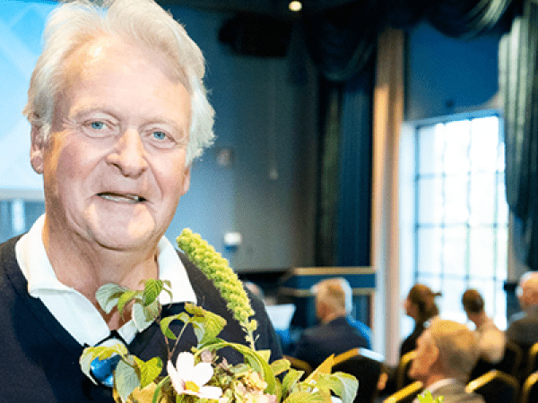Man med blommor i handen tittar leendes in i kameran