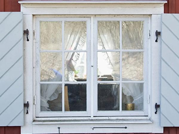 Ett fönster med vita luckor mot en röd furuvägg