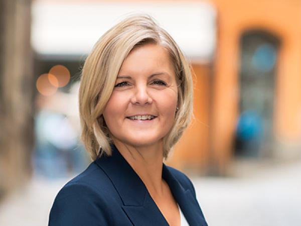 Kvinna i blont hår och kavaj tittar in i kameran