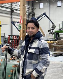Man med mörkt hår och rutig jacka står lutad med hand mot glasskivor