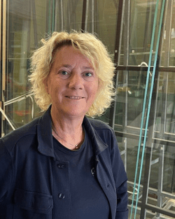Blond kvinna i svart tröja framför planglas 