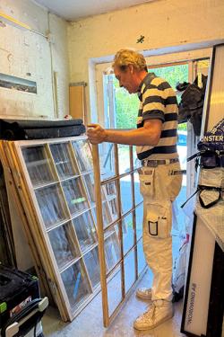 Man står i målarbyxor vid ett fönster