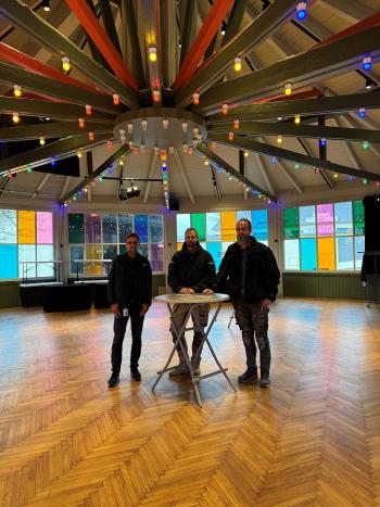 Tre män stor bredvid varandra i ett rum med färgade fönsterglas.