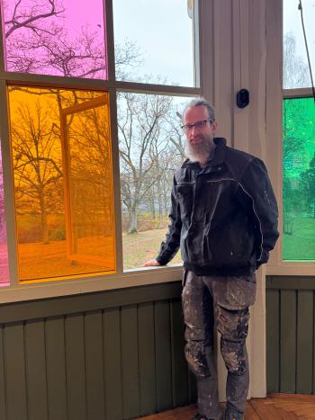 Man i arbetskläder står framför fönster i kulörta färger