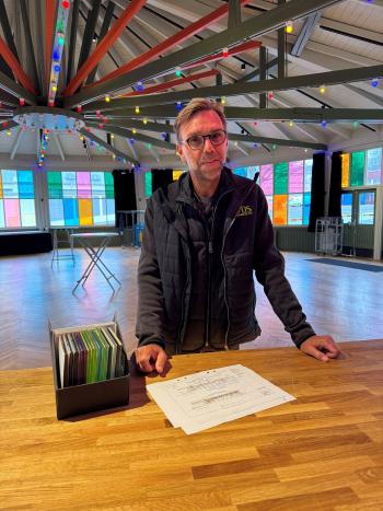 En man med svart jacka och glasögon står vid bord med provbitar av färgat glas.